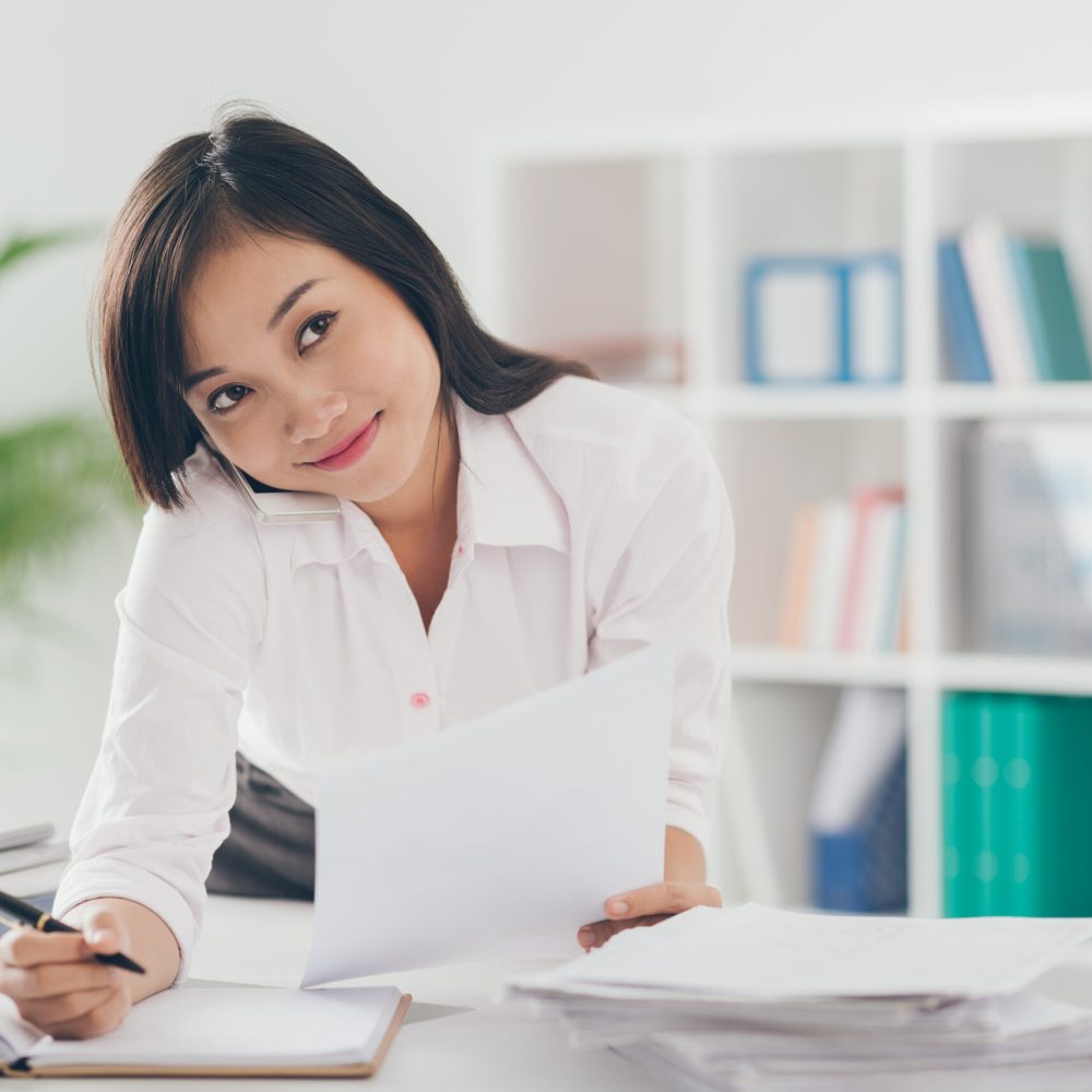 Pretty Asian manager talking on the phone and writing down in the office